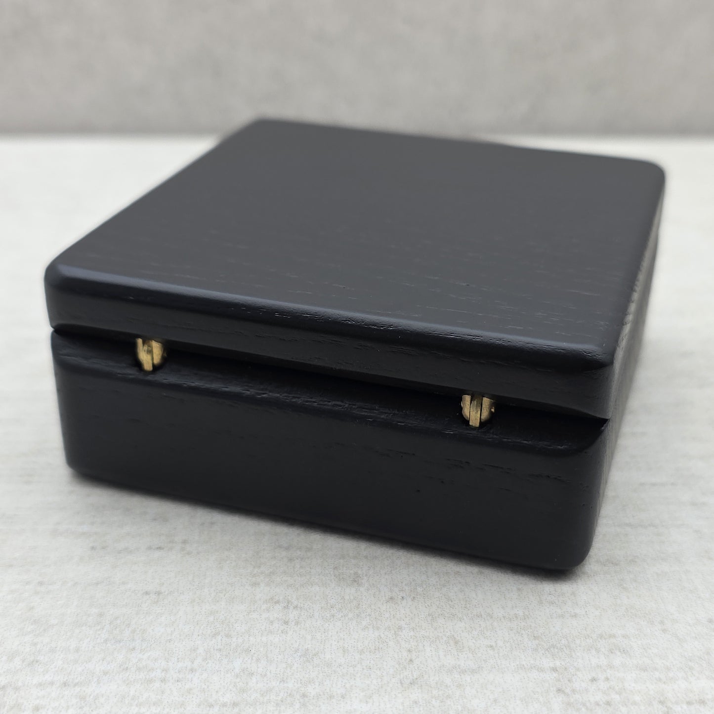 Rear view of closed black ash wood coin box highlighting two sturdy golden brass metal hinges for smooth opening and durability.