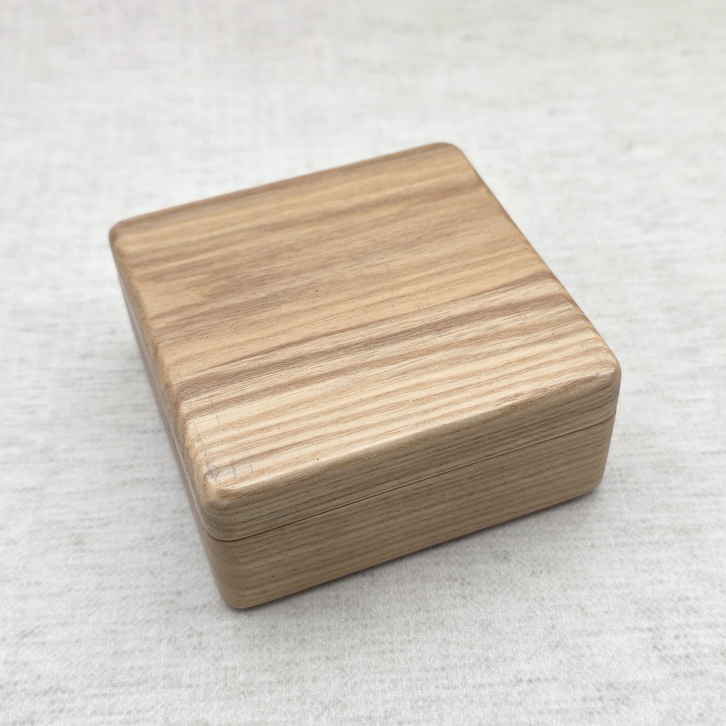 Closed natural ash wood gift box showing sleek rounded corners and prominent organic wood grain texture, modern minimalist design.