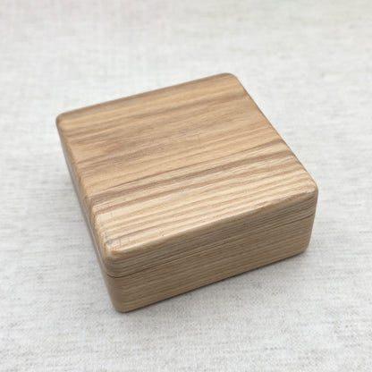 Closed natural ash wood gift box showing sleek rounded corners and prominent organic wood grain texture, modern minimalist design.