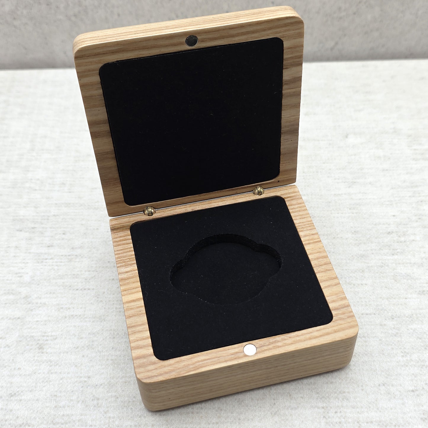 High angle view of open light-colored wooden gift box featuring matching black velvet-covered foam insert for challenge coins and medals.