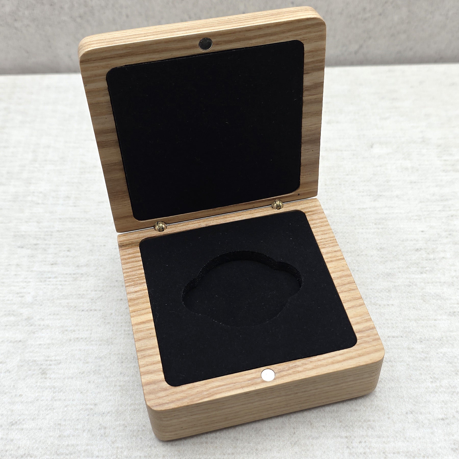 High angle view of open light-colored wooden gift box featuring matching black velvet-covered foam insert for challenge coins and medals.
