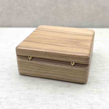 Rear view of closed light-colored wooden presentation box highlighting two sturdy golden brass metal hinges for smooth opening.