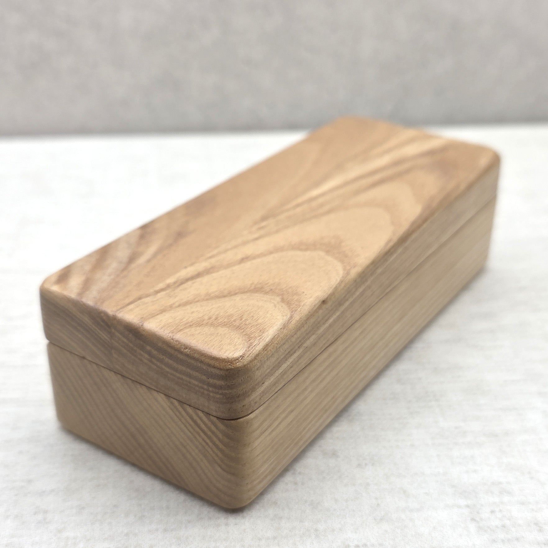 Closed solid ash wood display box side view showing natural wood grain texture and smooth rounded corners