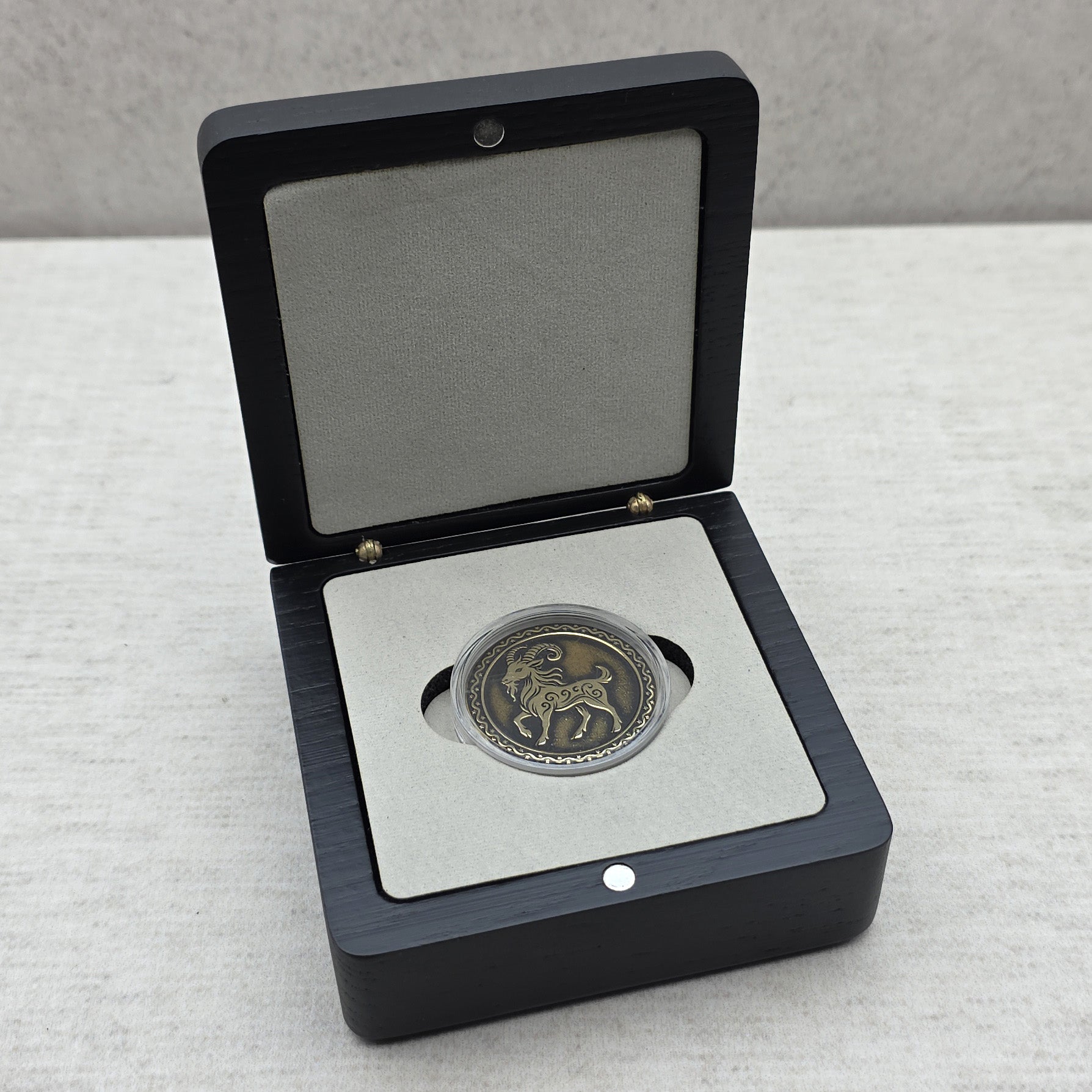 Handcrafted black ash wood gift box showing custom commemorative coin inside protective capsule on light gray velvet foam insert.