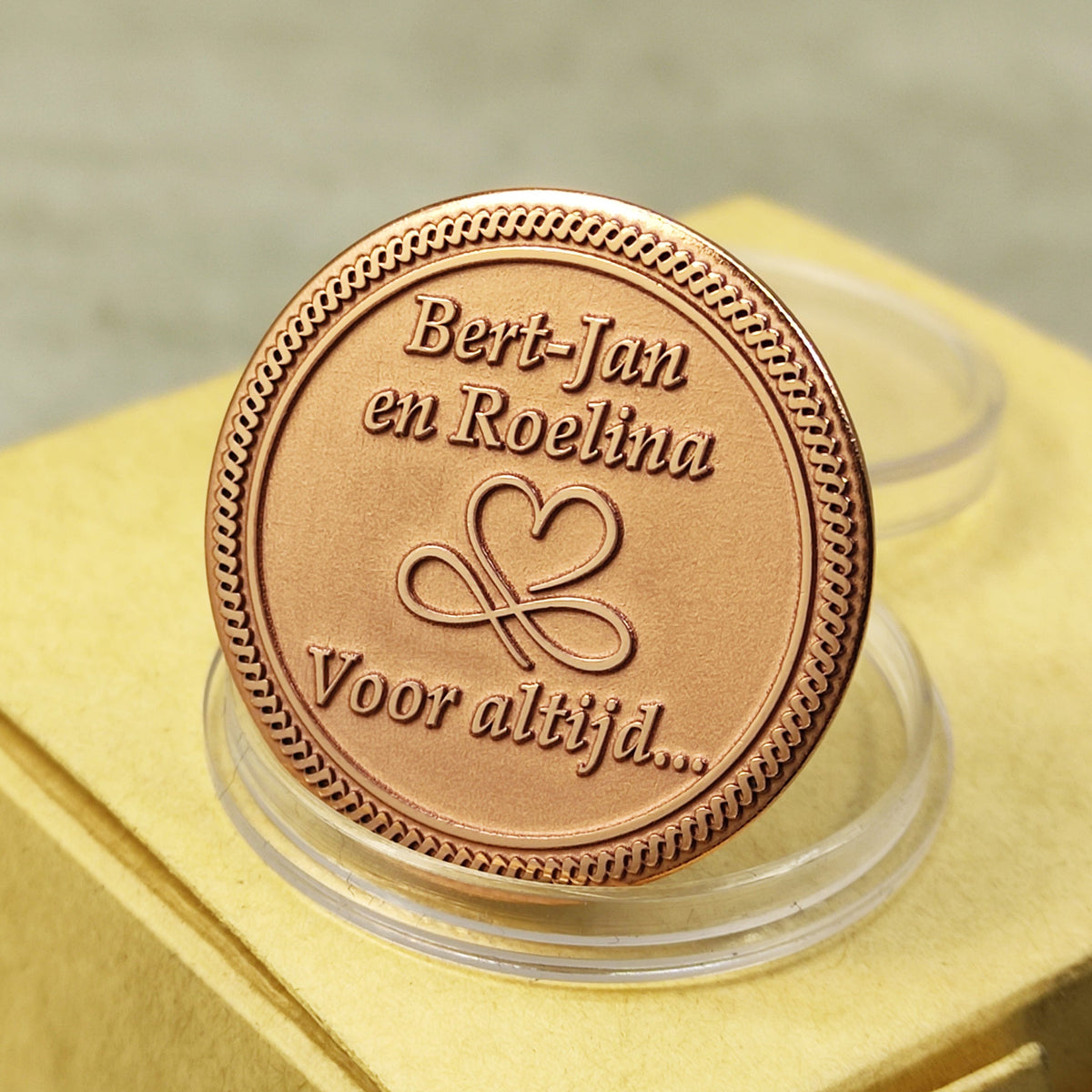 Close-up of a personalized copper coin with custom text and heart infinity symbol, featuring deep laser engraving and matte metallic finish.